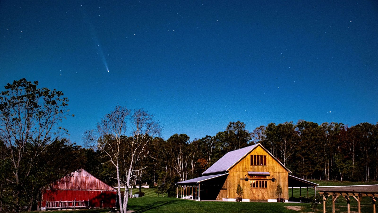 a blurred white streak in the night sky above a red barn