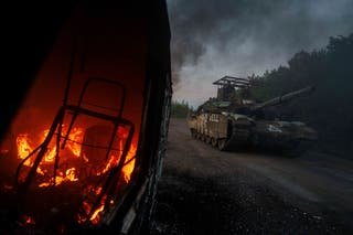 A Ukrainian tank goes past a burning car near the Russian-Ukrainian border in the Sumy region