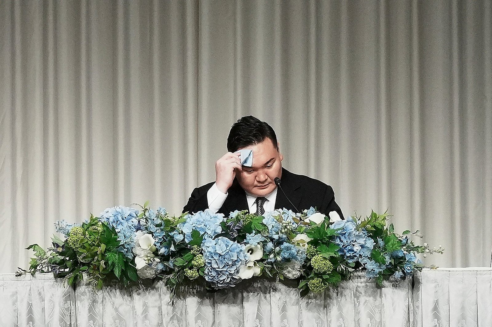 Hakuho Sho, a retired 'Yokozuna' or magnificent master of Sumo Hakuho, wipes his face during a press conference in Tokyo, Monday, June 9, 2025, to deliver a farewell message following the reported acceptance of his resignation and to outline his future plans. (AP Photo/Eugene Hoshiko)