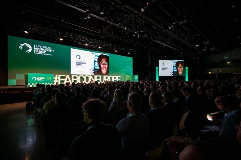 An image of an audience, sitting in a darkened room, watching a presentation at FabCon EU on a large screen.